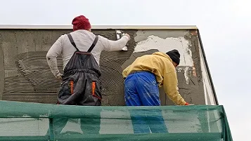 Dos albañiles revocando pared exterior